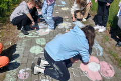 Uczniowie, posługując się organicznymi kredami,  malują na chodniku obrazy związane z naturą.